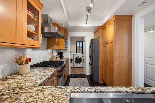 kitchen with freestanding refrigerator, high end stove, a raised ceiling, wall chimney exhaust hood, and washing machine and dryer