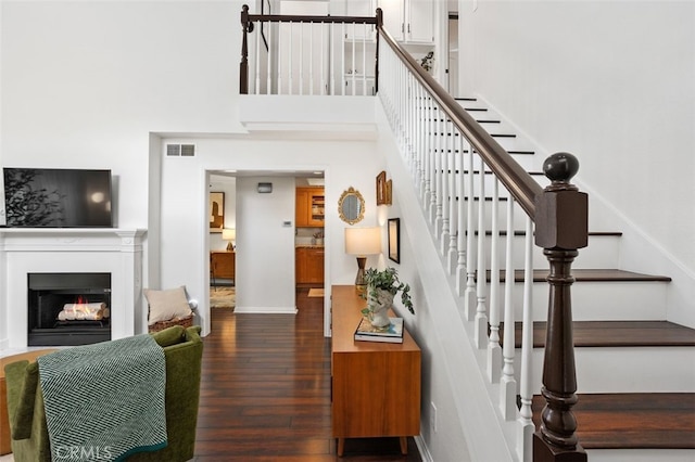 stairway with visible vents, baseboards, hardwood / wood-style floors, a warm lit fireplace, and a high ceiling