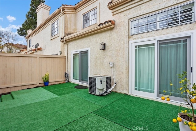 back of house with fence, stucco siding, a chimney, central air condition unit, and a lawn