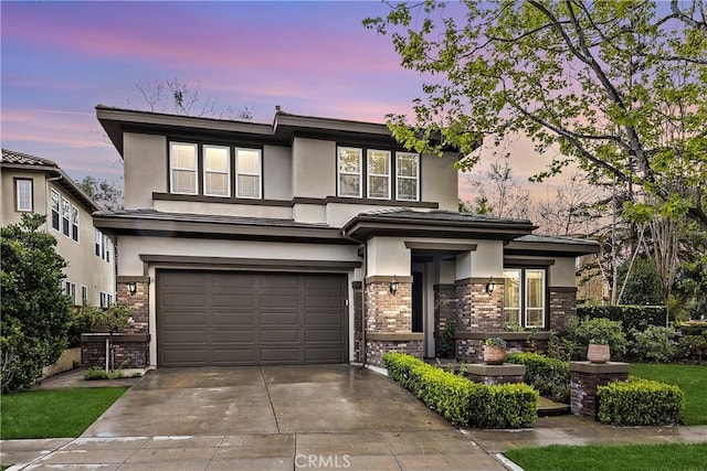 prairie-style house with an attached garage, brick siding, driveway, and stucco siding