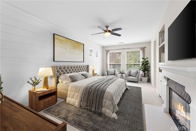 bedroom featuring a fireplace with flush hearth, a ceiling fan, and light carpet