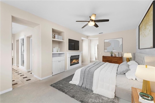 carpeted bedroom with a glass covered fireplace, a ceiling fan, and baseboards