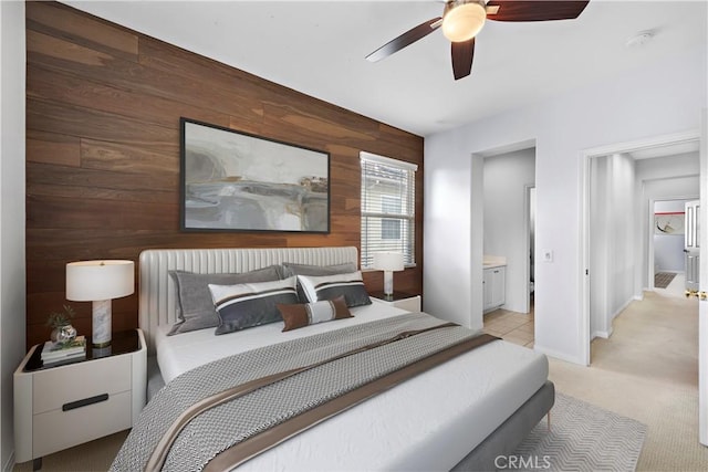 bedroom featuring wooden walls, connected bathroom, a ceiling fan, and light carpet