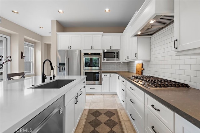 kitchen with custom exhaust hood, a sink, stainless steel appliances, white cabinets, and tasteful backsplash