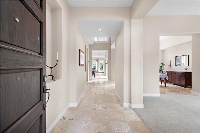 hallway featuring baseboards and light colored carpet