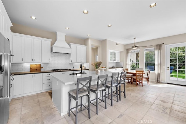 kitchen with premium range hood, a kitchen island with sink, a sink, appliances with stainless steel finishes, and a breakfast bar area