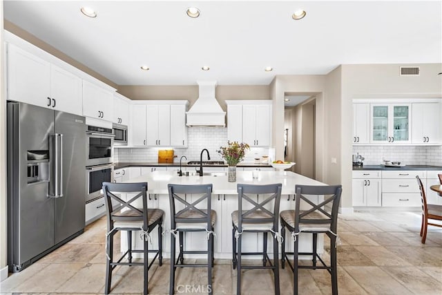 kitchen featuring visible vents, a breakfast bar area, custom range hood, appliances with stainless steel finishes, and white cabinets