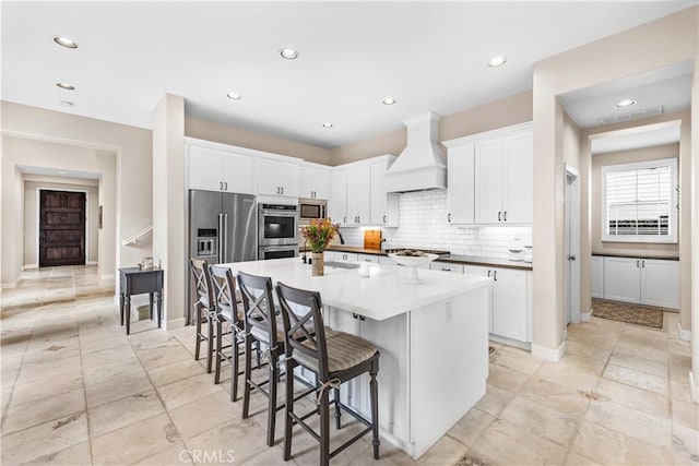 kitchen featuring visible vents, an island with sink, custom range hood, a kitchen breakfast bar, and stainless steel appliances