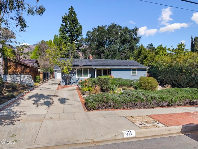 ranch-style home featuring a chimney, roof mounted solar panels, driveway, and an attached garage