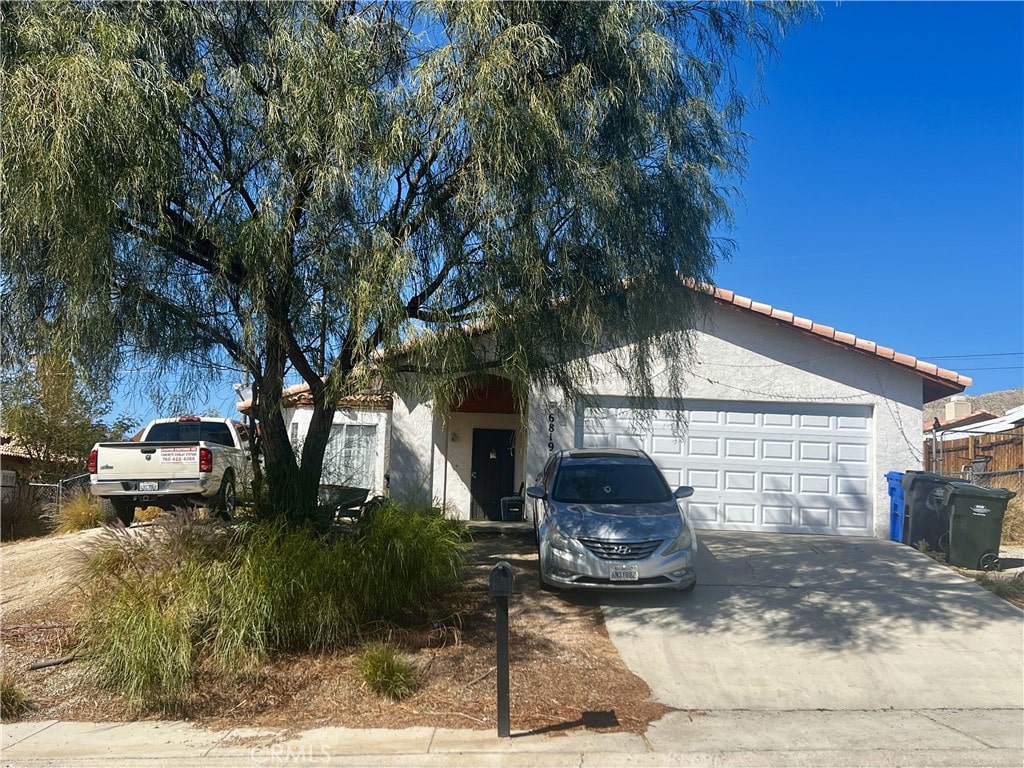 single story home with a tiled roof, an attached garage, driveway, and stucco siding