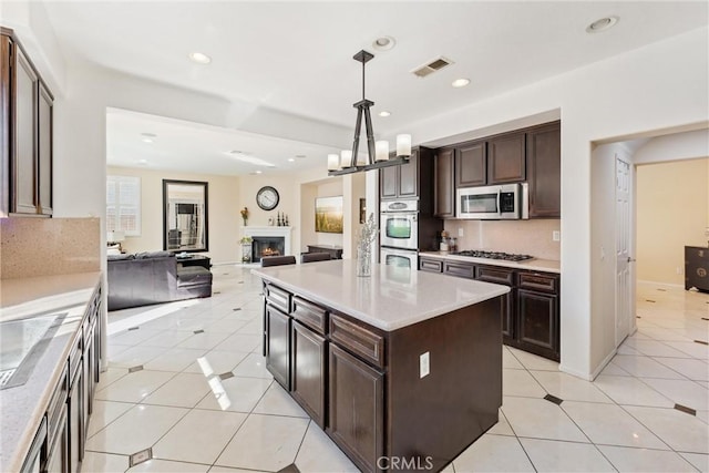 kitchen featuring visible vents, dark brown cabinetry, light tile patterned floors, a warm lit fireplace, and stainless steel appliances