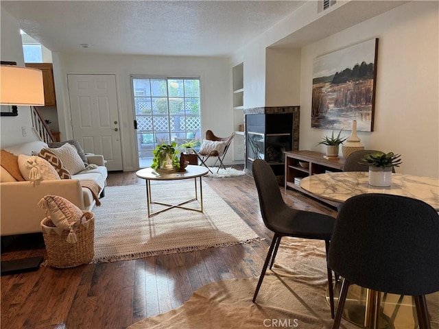 living area featuring built in features, a textured ceiling, stairway, wood-type flooring, and a tile fireplace