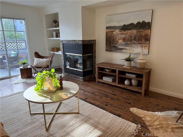 living room featuring a tiled fireplace, built in shelves, baseboards, and hardwood / wood-style floors