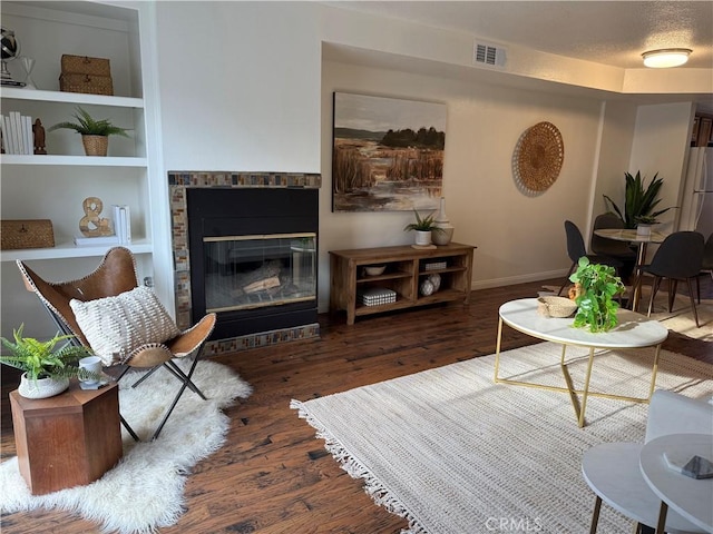 living area with built in shelves, wood finished floors, visible vents, a textured ceiling, and a glass covered fireplace