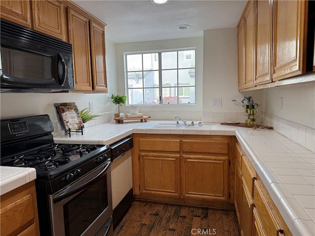 kitchen featuring tile countertops, stainless steel range with gas cooktop, black microwave, and white dishwasher