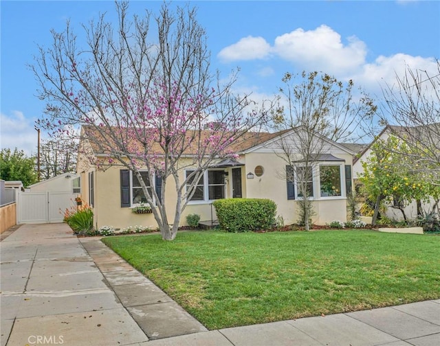 ranch-style house with a front lawn, fence, stucco siding, driveway, and a gate