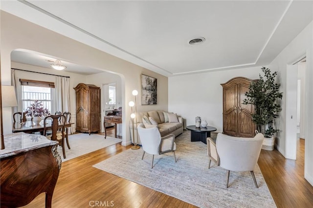 living area with visible vents, arched walkways, and light wood finished floors