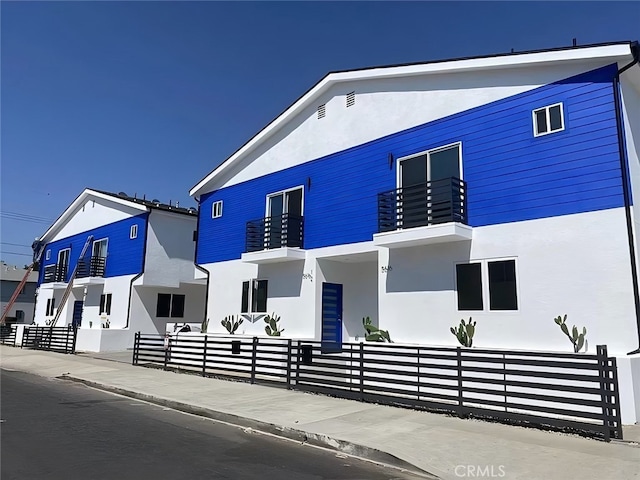 modern home featuring a fenced front yard, a balcony, and stucco siding