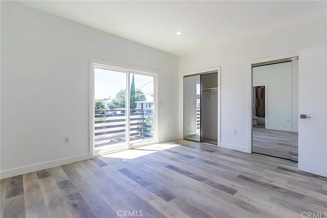 unfurnished bedroom featuring access to outside, wood finished floors, baseboards, and two closets