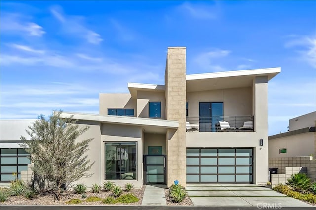 contemporary house with stucco siding, a balcony, a garage, and driveway