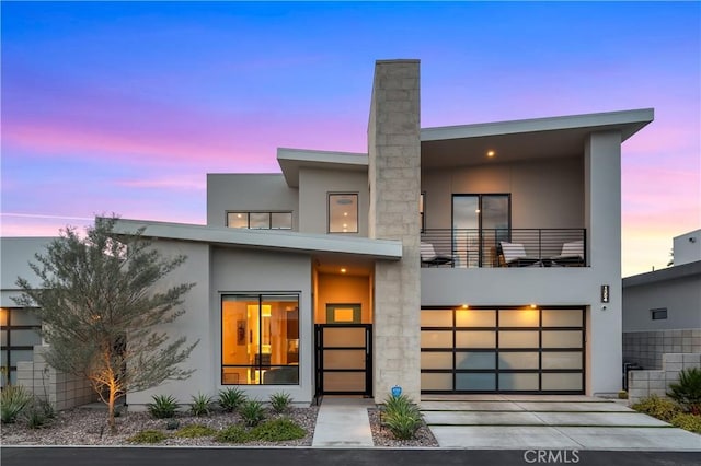 back of house at dusk with a garage, stucco siding, driveway, and a balcony