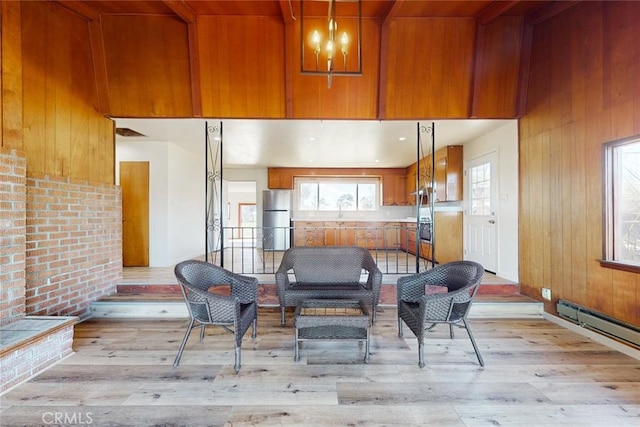 living area featuring a notable chandelier, light wood-style flooring, wood walls, and a baseboard radiator