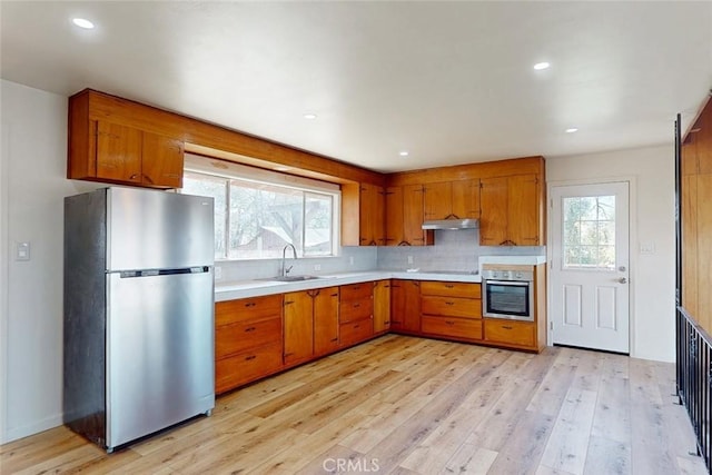 kitchen with light wood-type flooring, brown cabinets, a sink, appliances with stainless steel finishes, and light countertops