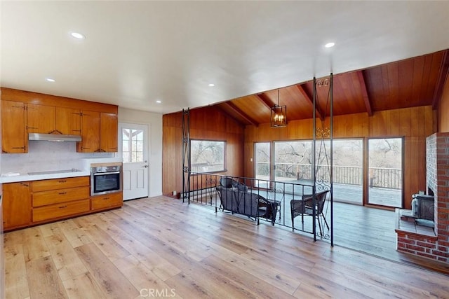 kitchen featuring oven, under cabinet range hood, brown cabinetry, light wood finished floors, and black electric stovetop