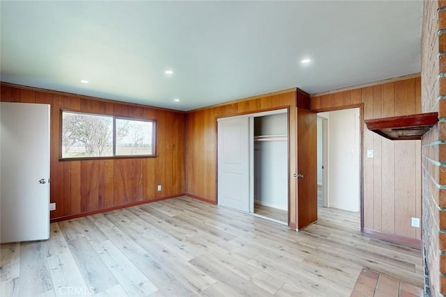 unfurnished bedroom with wooden walls, recessed lighting, light wood-type flooring, and a closet