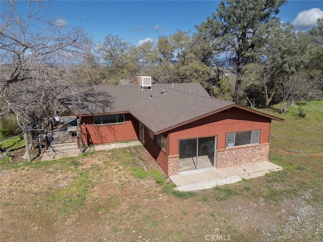 rear view of house featuring brick siding, a patio area, cooling unit, and roof with shingles