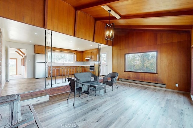 sitting room with light wood finished floors, vaulted ceiling with beams, wood walls, baseboard heating, and a notable chandelier