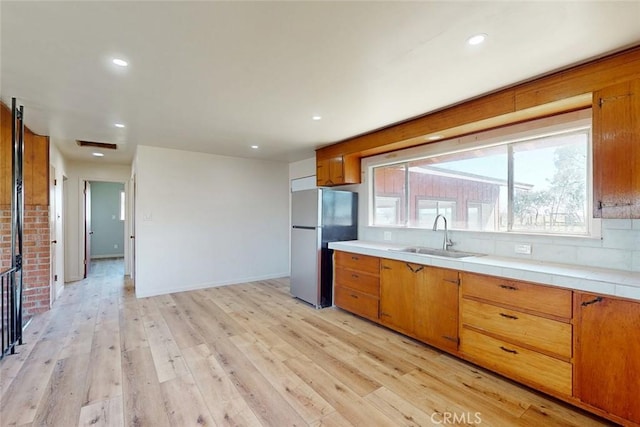 kitchen with a sink, light wood-style flooring, light countertops, and freestanding refrigerator