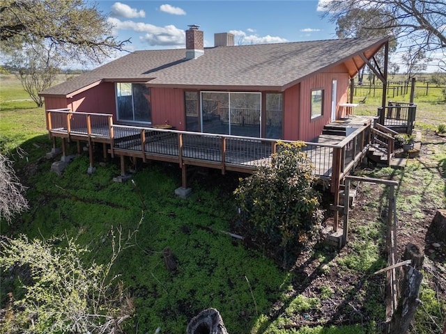 back of property with a chimney, a wooden deck, and roof with shingles