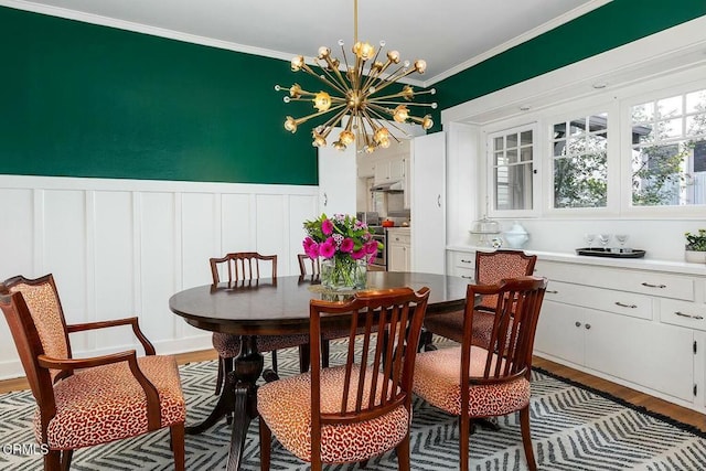 dining area featuring crown molding, wood finished floors, wainscoting, and a chandelier