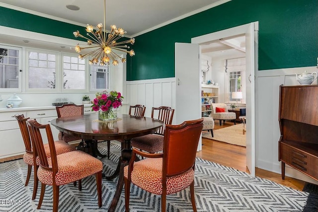 dining room featuring a wainscoted wall, wood finished floors, a notable chandelier, and ornamental molding