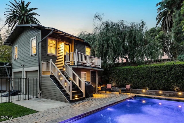 back of property at dusk featuring a fenced in pool, fence, stairs, a patio area, and an attached garage