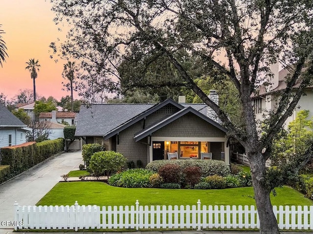 craftsman house with a chimney, concrete driveway, a front lawn, and fence