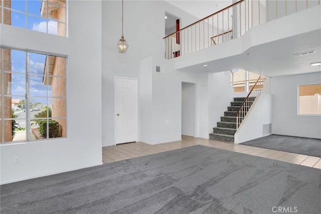 unfurnished living room with tile patterned floors, stairway, visible vents, and carpet floors