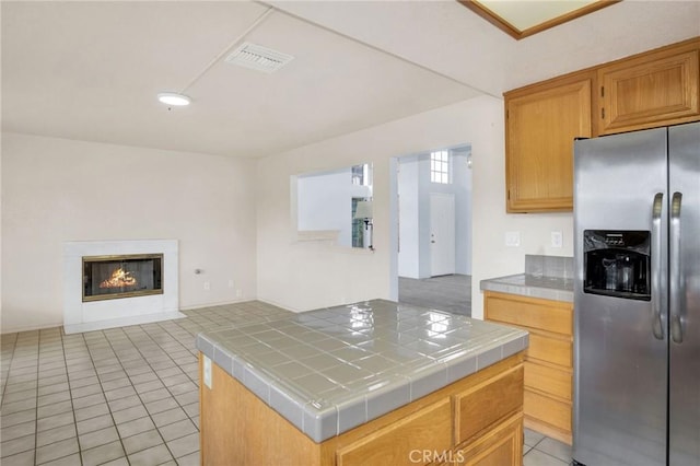 kitchen with visible vents, tile counters, open floor plan, light tile patterned floors, and stainless steel refrigerator with ice dispenser