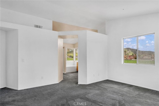 empty room with dark colored carpet, visible vents, baseboards, and vaulted ceiling