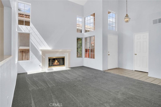 unfurnished living room with a fireplace with flush hearth, visible vents, carpet floors, and a towering ceiling