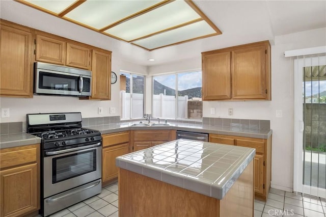 kitchen with a sink, a mountain view, appliances with stainless steel finishes, light tile patterned floors, and tile counters