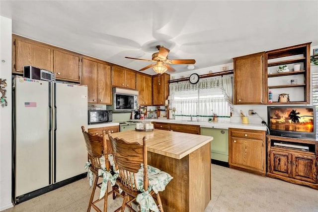 kitchen featuring brown cabinetry, freestanding refrigerator, ceiling fan, black microwave, and stainless steel microwave