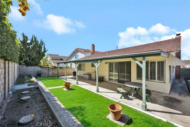 back of property with a fenced backyard, a yard, a chimney, and a patio