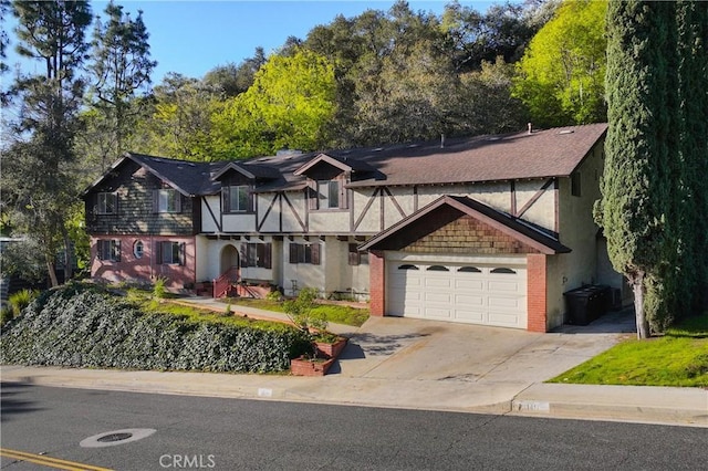 tudor house featuring stucco siding, brick siding, a garage, and concrete driveway