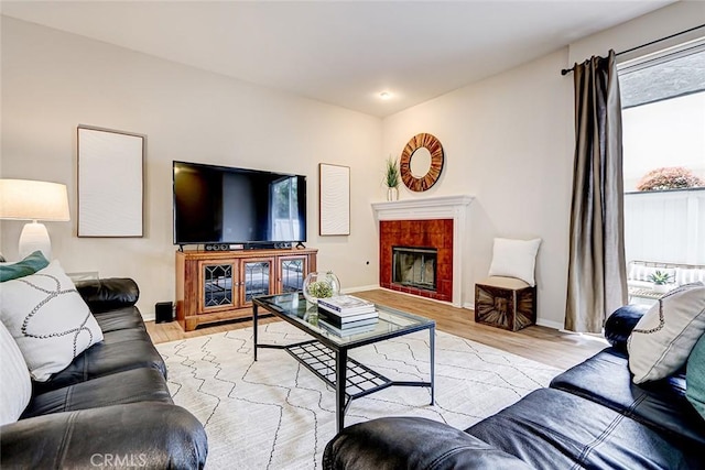 living area featuring baseboards, light wood-style floors, and a tiled fireplace