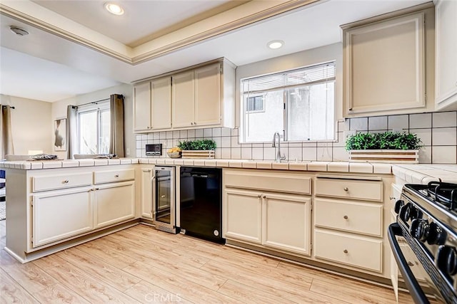 kitchen featuring light wood-type flooring, black appliances, a sink, cream cabinets, and a peninsula