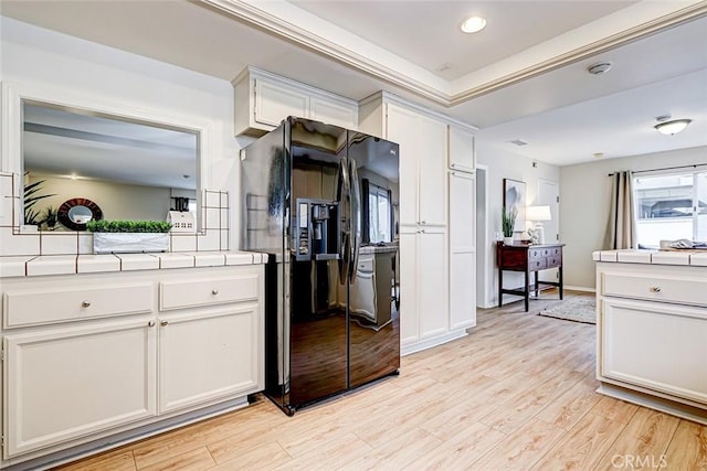 kitchen with black fridge with ice dispenser, white cabinetry, light wood-type flooring, and tile counters