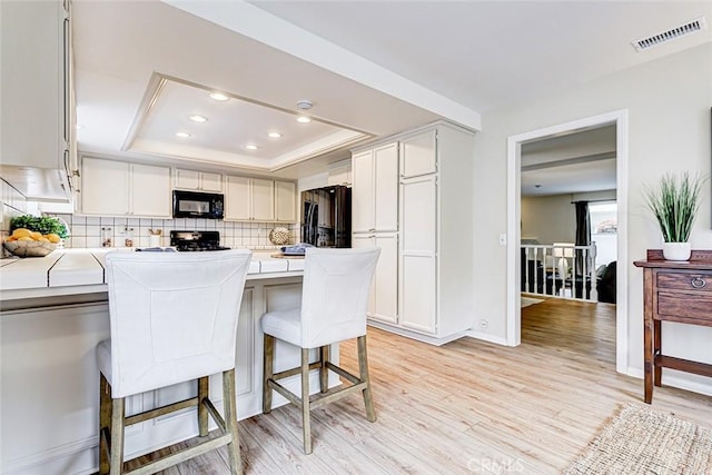 kitchen with visible vents, a tray ceiling, black appliances, light countertops, and light wood-type flooring