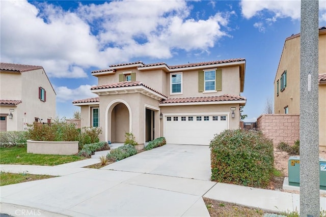 mediterranean / spanish-style house featuring fence, a tile roof, concrete driveway, stucco siding, and a garage